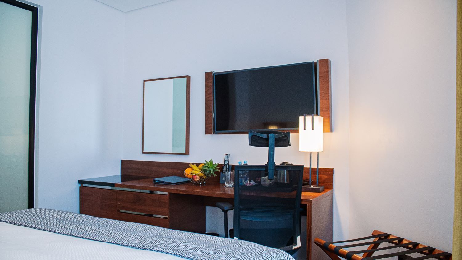 Una habitación de hotel con cama, escritorio, silla, televisor y lámpara.