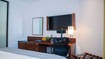 Una habitación de hotel con cama, escritorio, silla, televisor y lámpara.