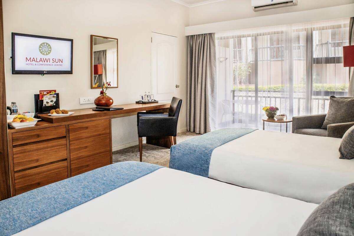 A hotel room with two beds, a desk, a chair, a TV, and a window with curtains.