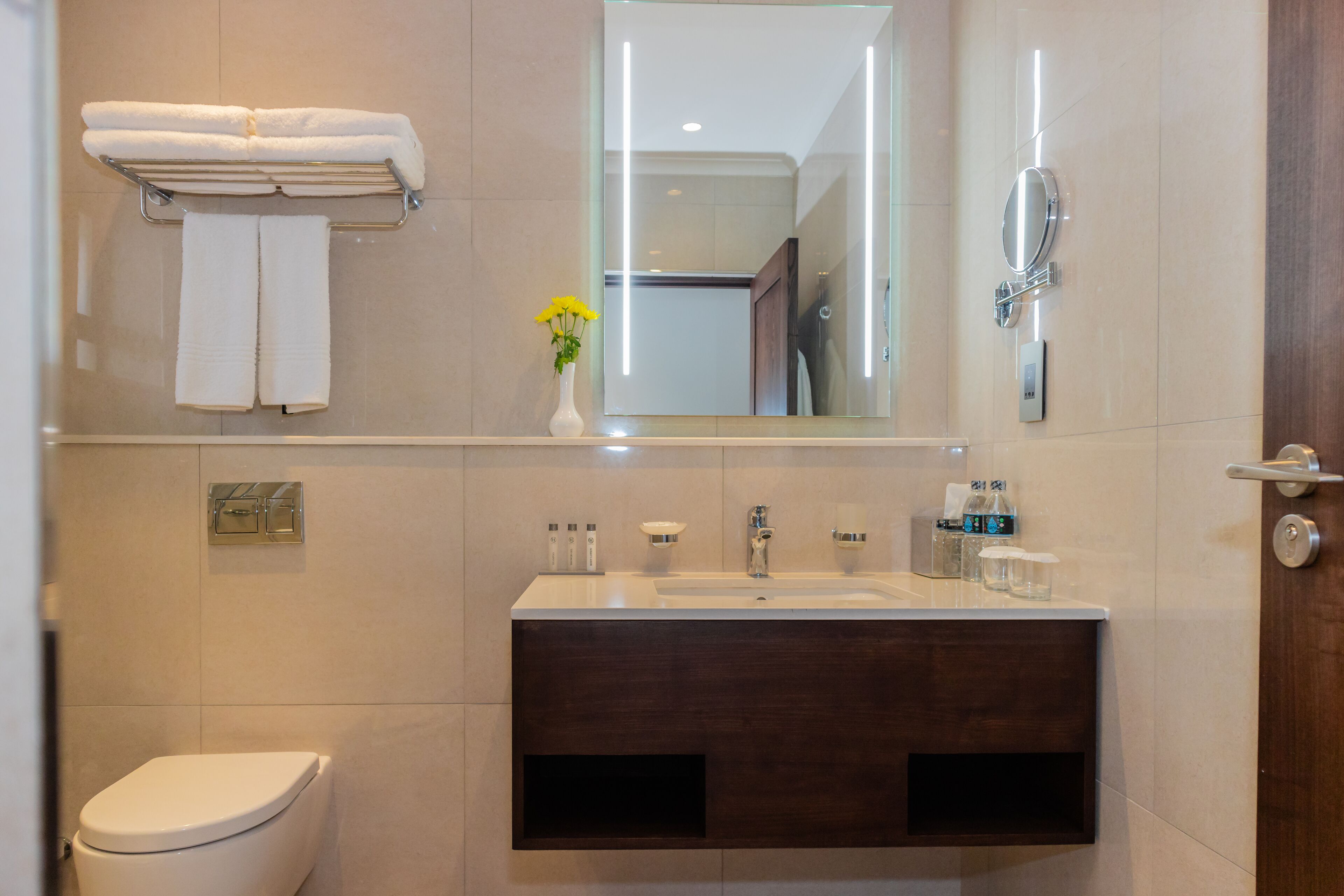 A modern bathroom with a toilet, a sink with a mirror above it, and a towel rack with folded towels.