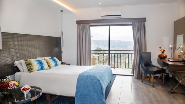 Quarto de hotel moderno com uma cama grande, uma escrivaninha, uma cadeira e uma varanda com vista para a cidade.