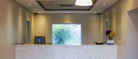 Un área de recepción con un mostrador de diseño en patrón de espiga, iluminación colgante y una gran obra de arte abstracta en la pared.