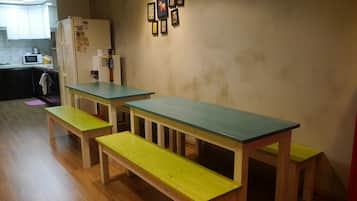 A small kitchen with wooden tables and benches, a refrigerator, and a microwave.