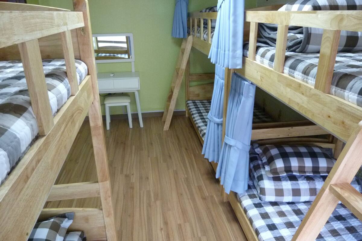 Une chambre avec un lit superposé, un bureau et une chaise, un plancher en bois et une literie à carreaux.
