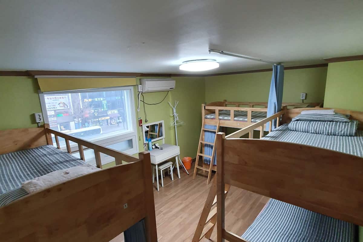 Une chambre de dortoir avec des lits superposés, un bureau et une fenêtre donnant sur la rue.