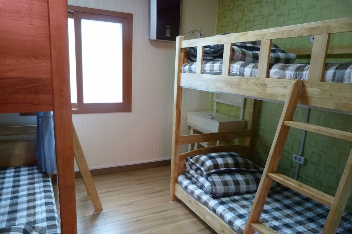 Une chambre avec un lit superposé, une fenêtre, un plancher en bois et un bureau.