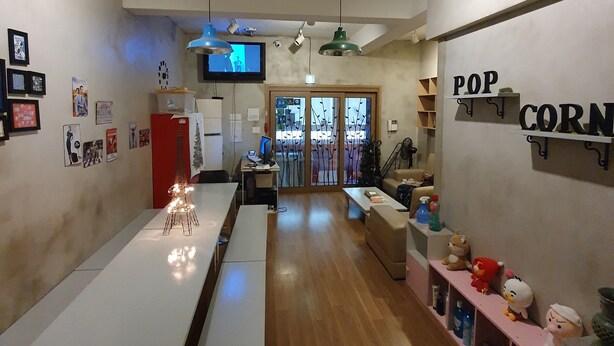 A modern kitchen with a long counter, a dining area with a bench, and a cozy seating area with plush toys. - Popcorn Hostel Nampodong (Busan)