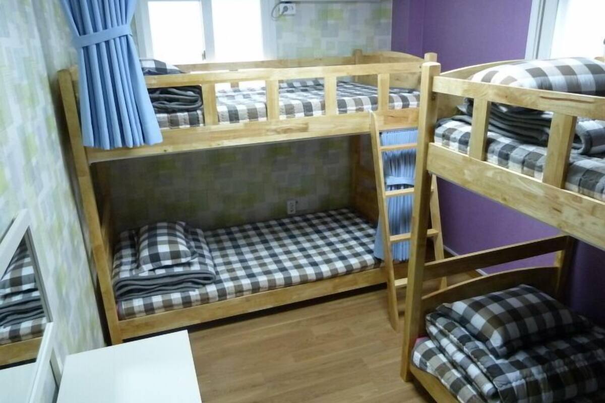 Une chambre avec un lit superposé, dotée de draps à carreaux et d’une échelle en bois.