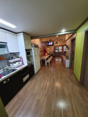 A modern kitchen with white cabinets, a refrigerator, and a microwave. There is a wooden bench and a television mounted on the wall.