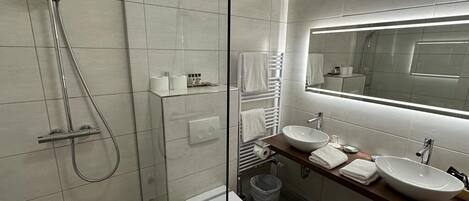Un baño moderno con ducha de vidrio, inodoro y dos lavamanos con espejos.