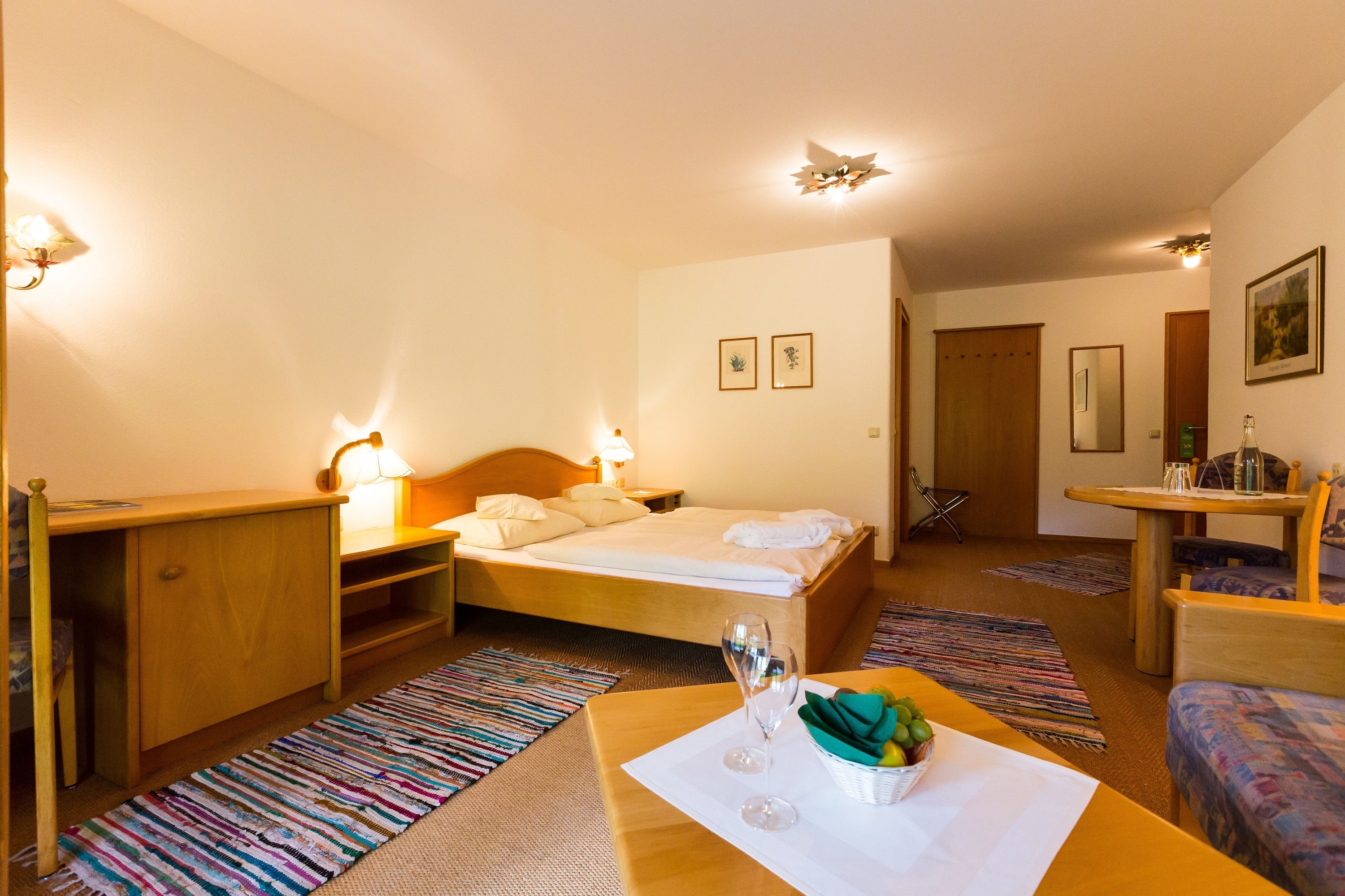 Een hotelkamer met een bed, nachtkastje, lamp en een klein zithoekje met een tafel en stoel.