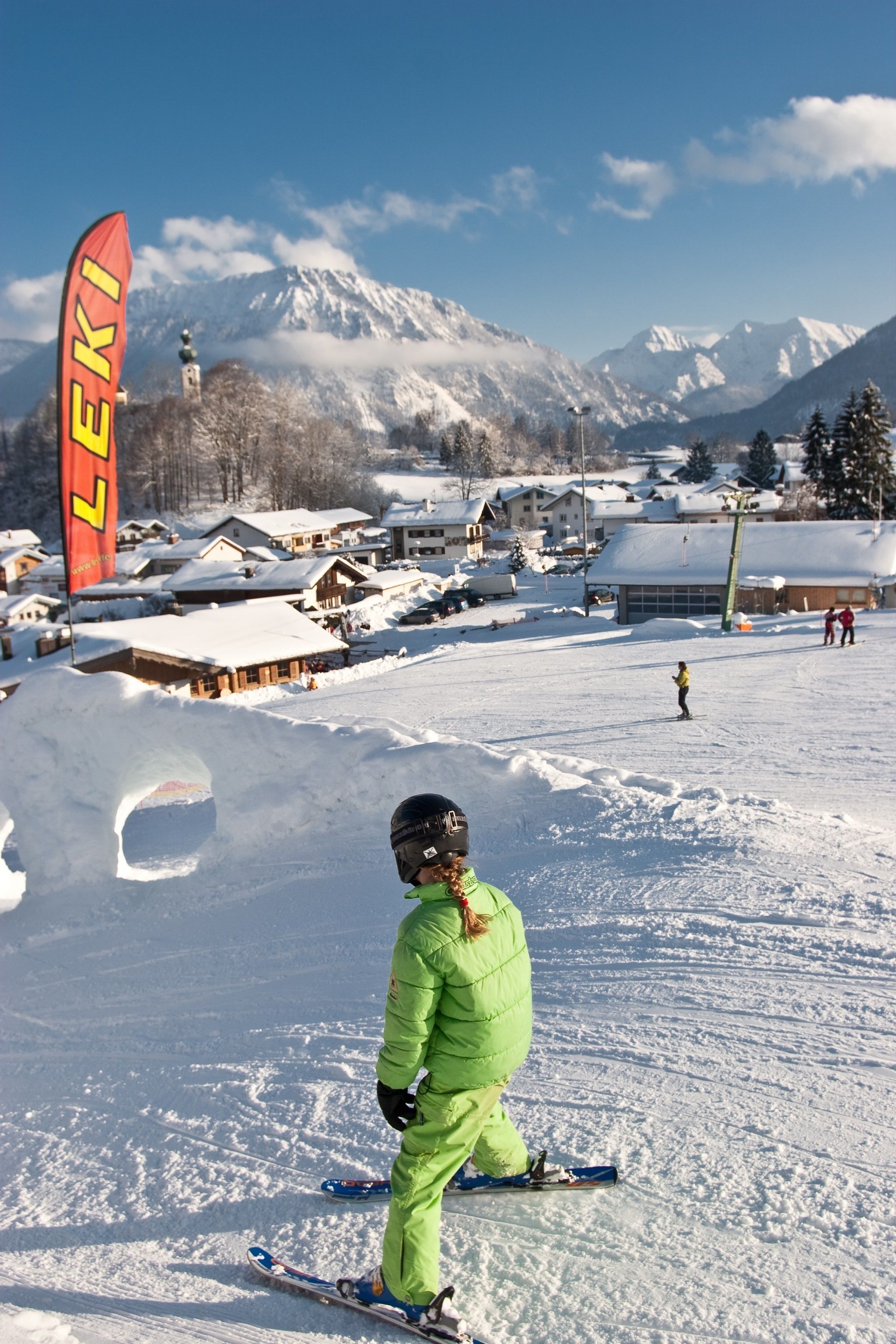 A ski resort with snow-covered mountains in the background, a ski lift, and a person skiing.