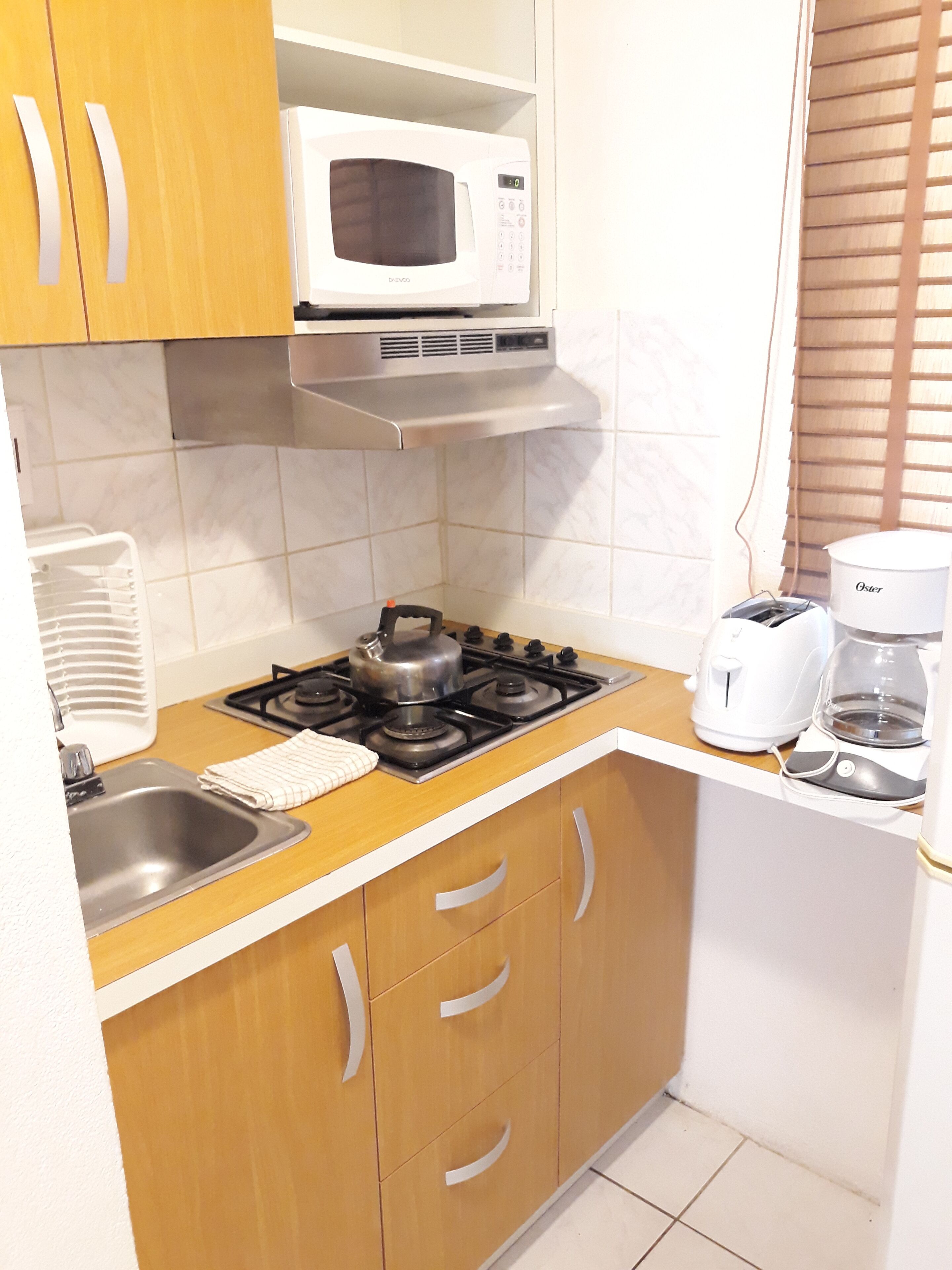 A compact kitchen with a gas stove, a microwave, a kettle, a toaster, and a coffee maker.