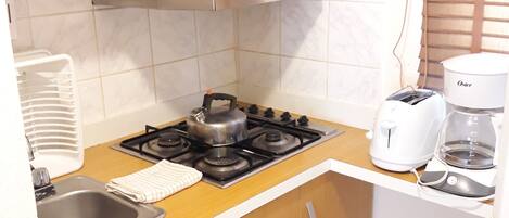 A compact kitchen with a gas stove, a microwave, a kettle, a toaster, and a coffee maker.