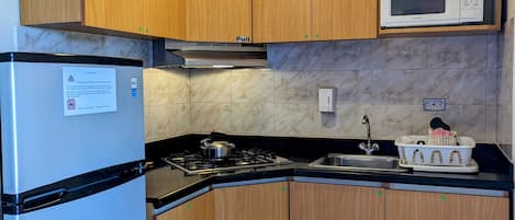 A compact kitchen with wooden cabinets, a stainless steel refrigerator, a microwave, and a gas stove.