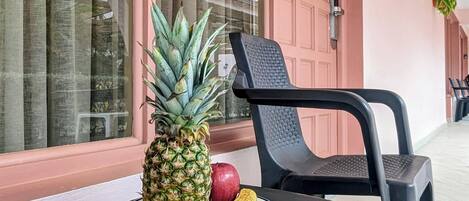 A table with a plate of pineapple, banana, and apple, a black chair, and a pink door with the number 105.