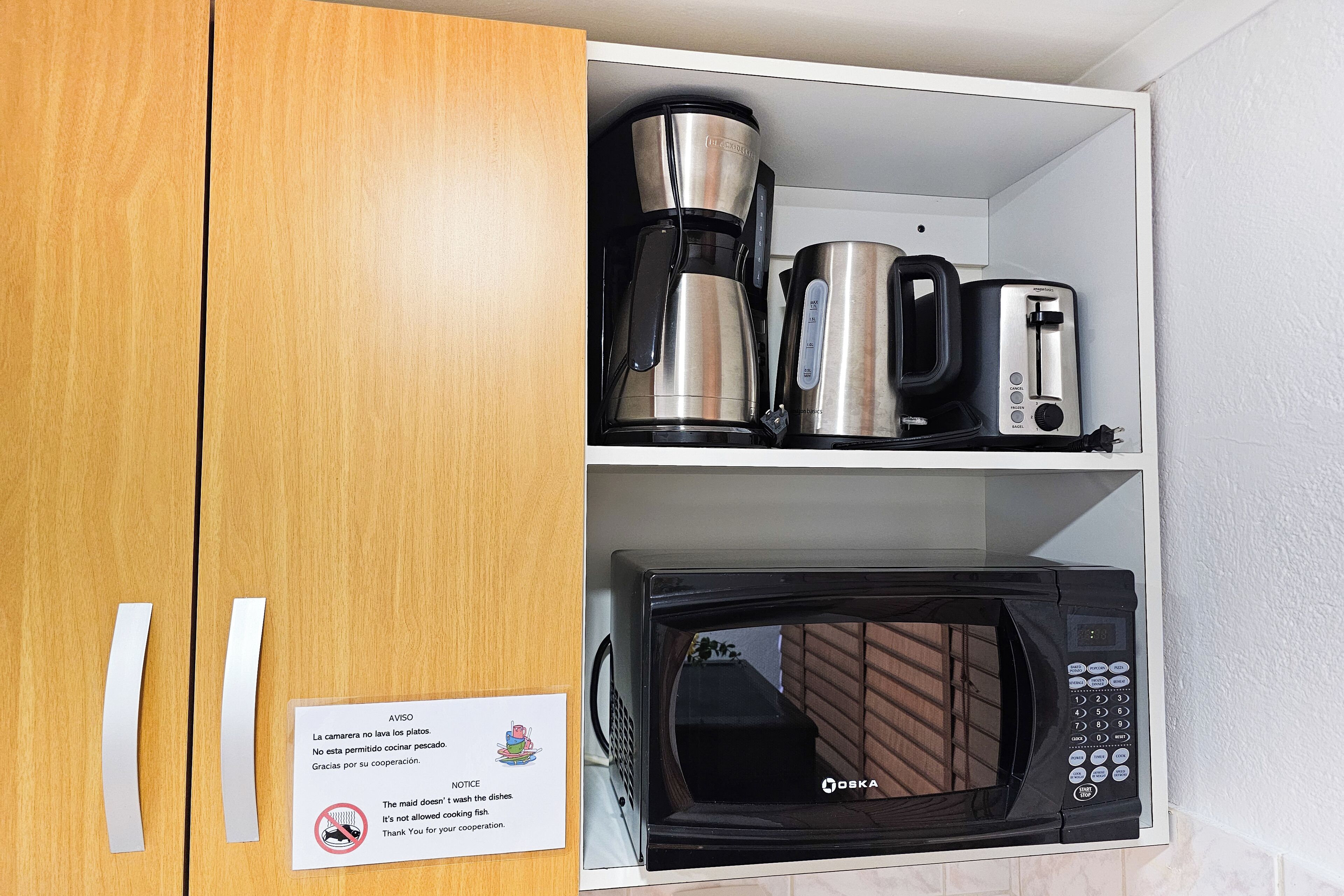 Eine Küchenzeile mit Kaffeemaschine, Toaster und Mikrowelle. An der Wand befindet sich ein Hinweis zu den Küchenregeln.