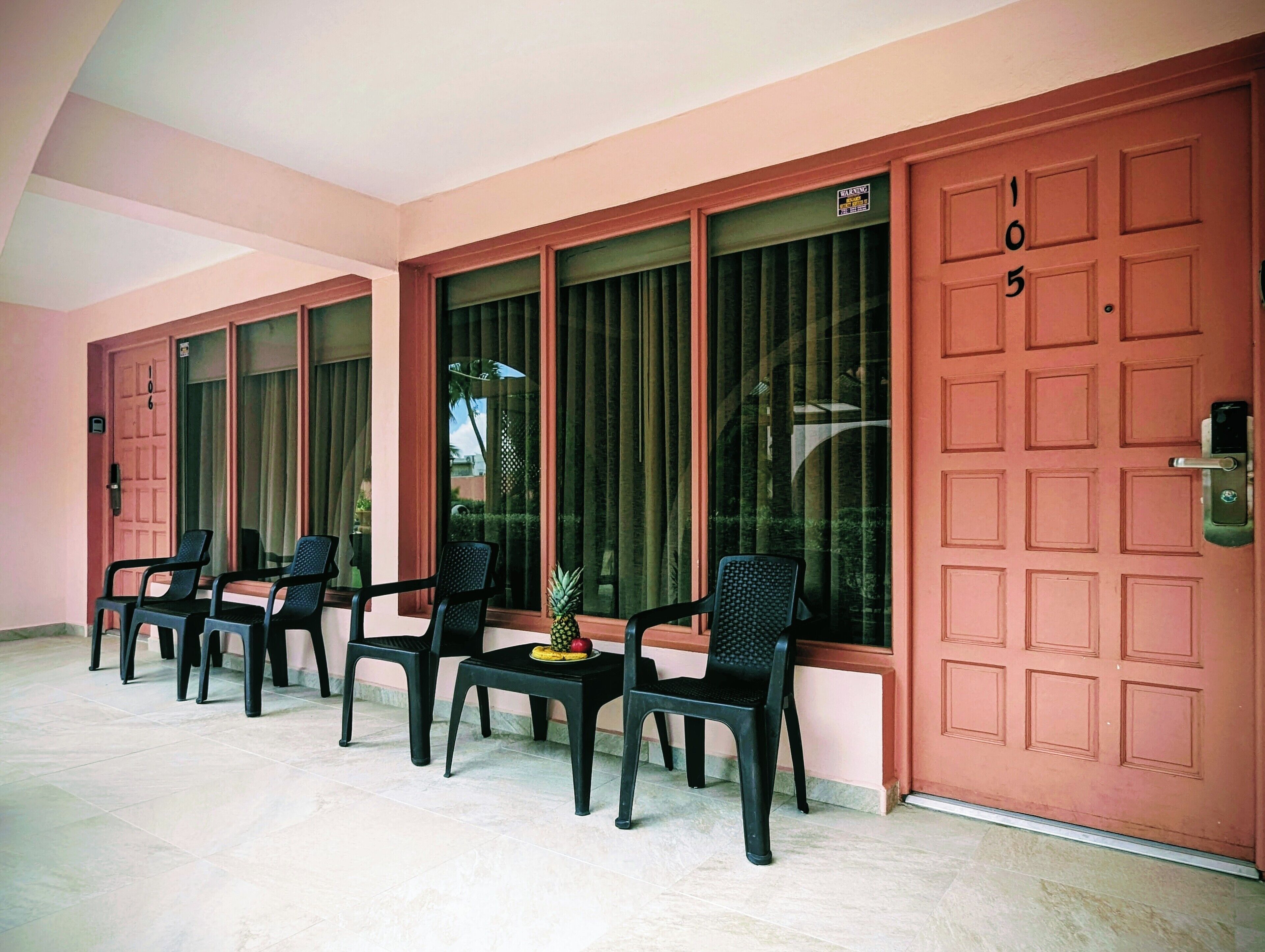 A hotel room with a large window, a door with the number 105, and several plastic chairs arranged in front of the window.