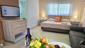 A hotel room with a bed, bedside tables, a TV, a dining table with flowers and fruit, and a sofa. - Sasaki Apartments (Noord)