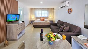 A hotel room with a bed, a sofa, a TV, a desk with a phone, a table with a bottle, glasses, and flowers. - Sasaki Apartments (Noord)