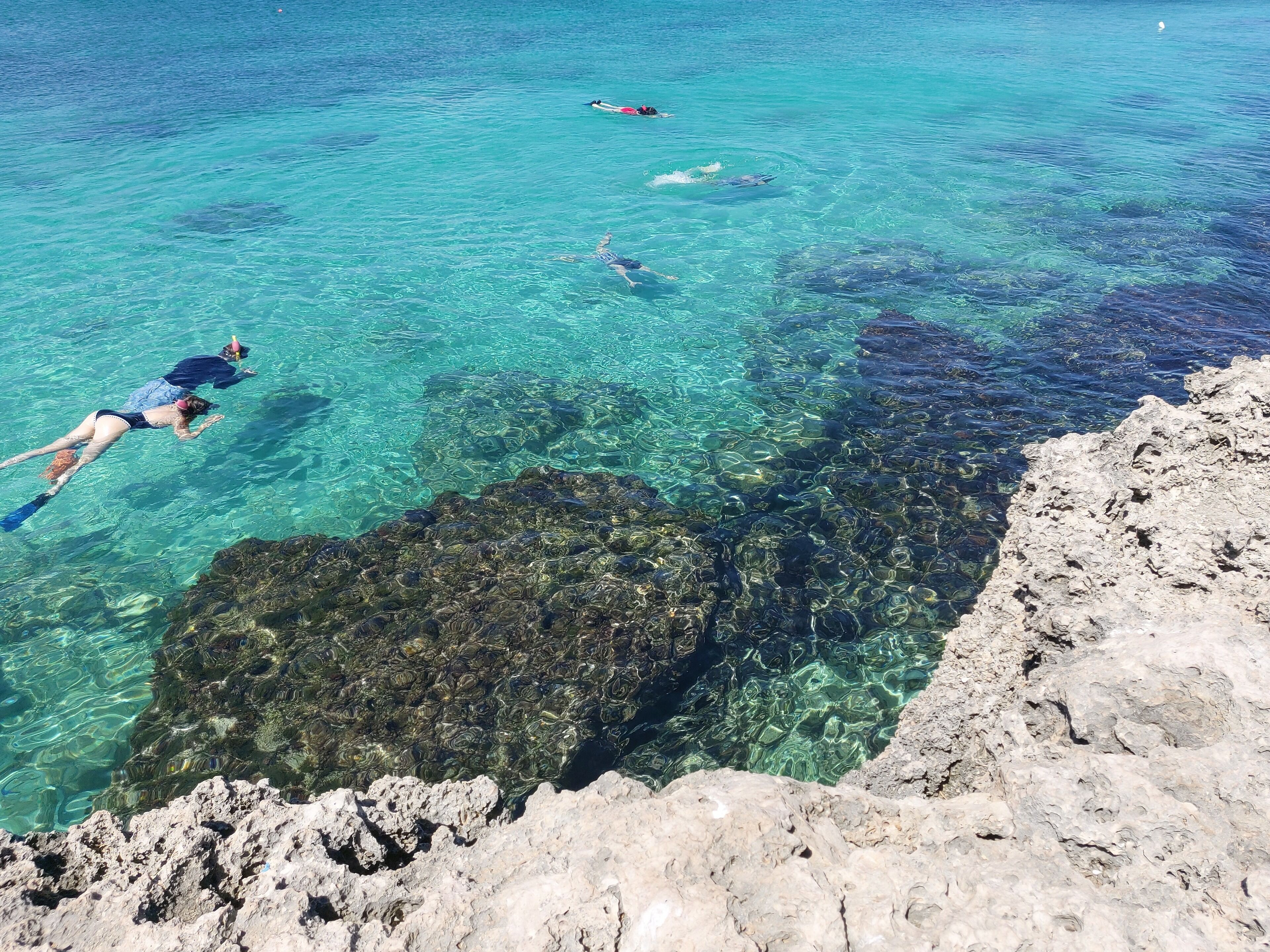 Un mar azul cristalino con formaciones rocosas y personas nadando.