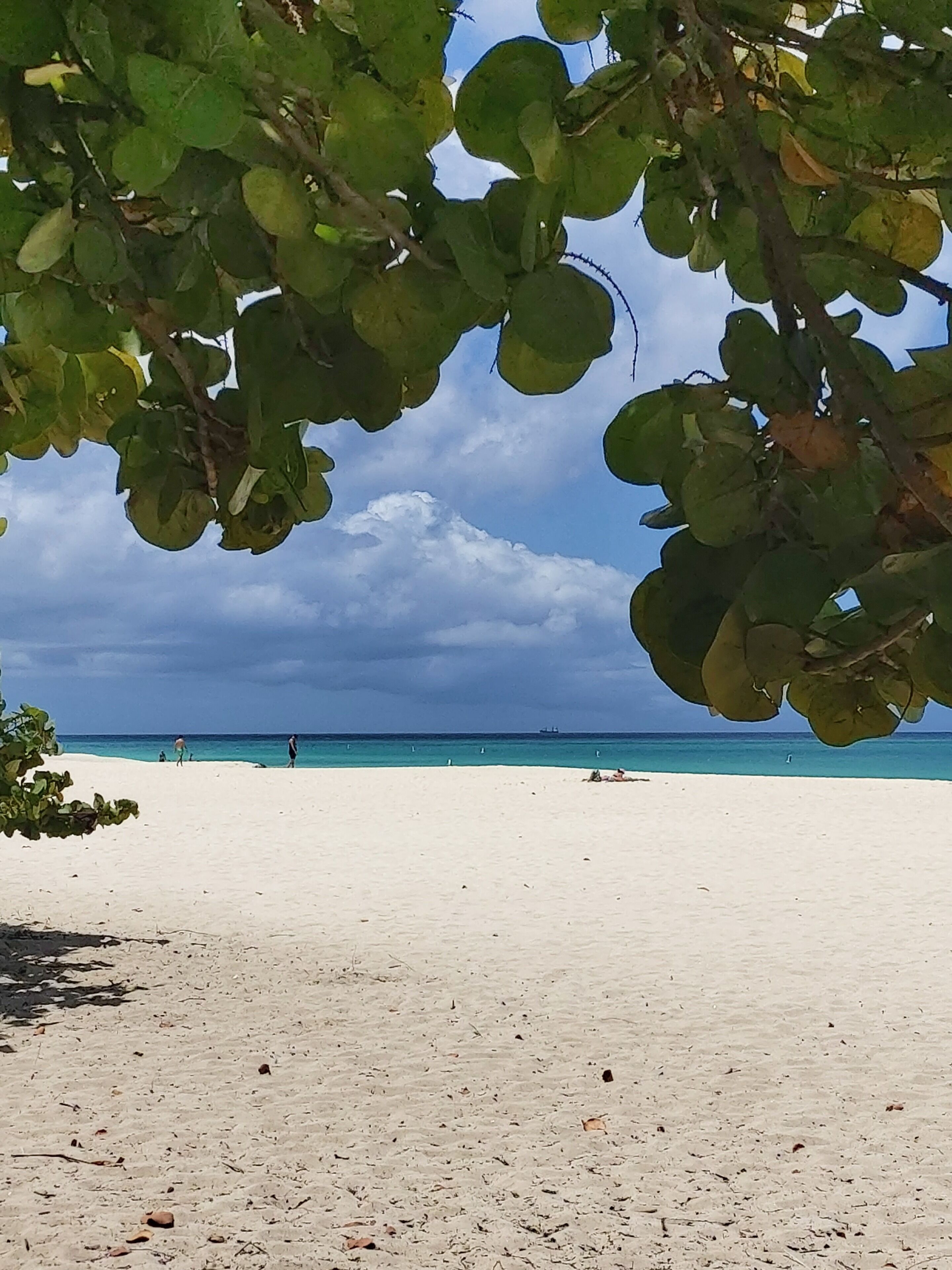 A beach with clear turquoise water, white sand, and a few people in the distance.