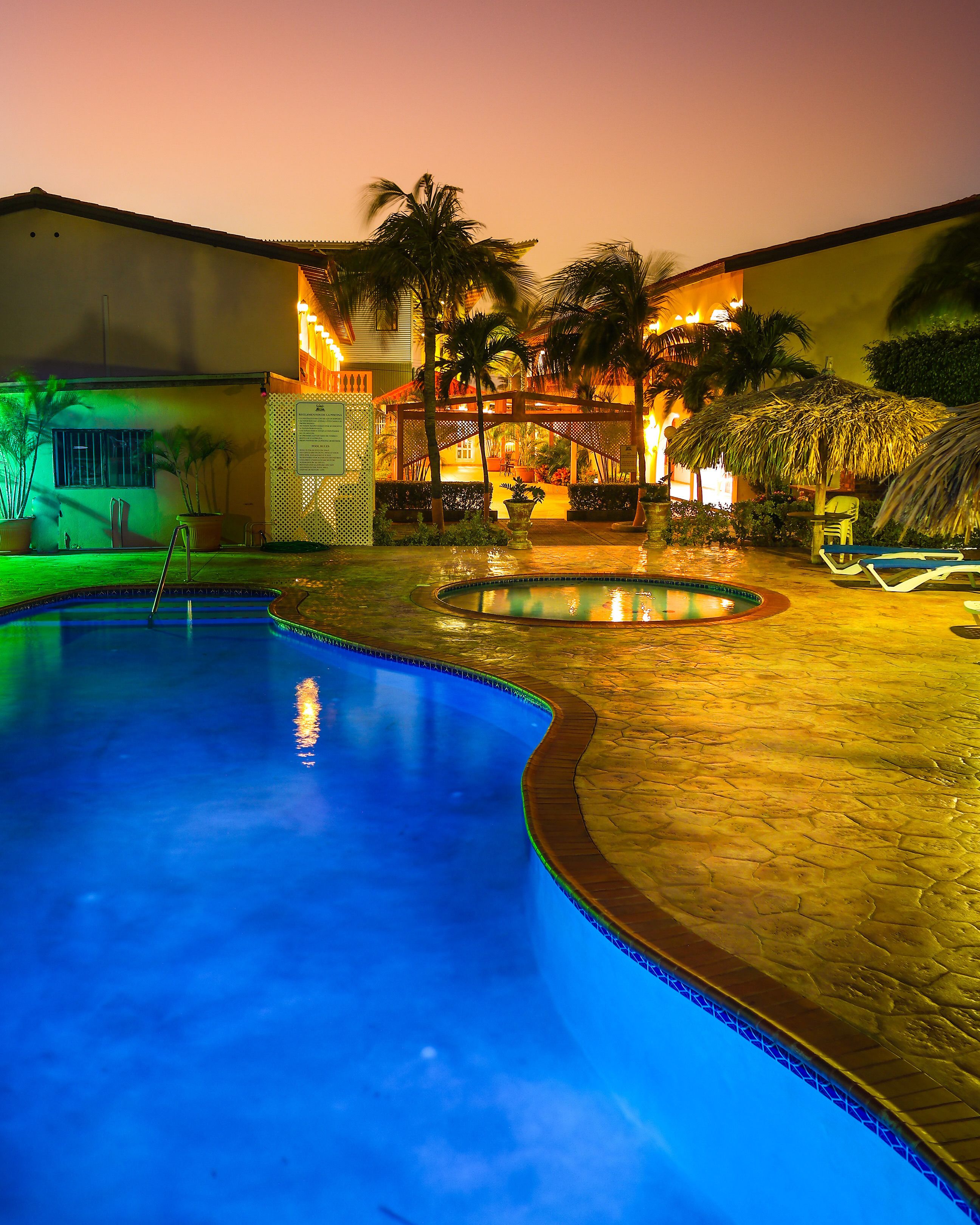 Una piscina con cubierta de madera, un área de estar techada con techo de paja y palmeras.