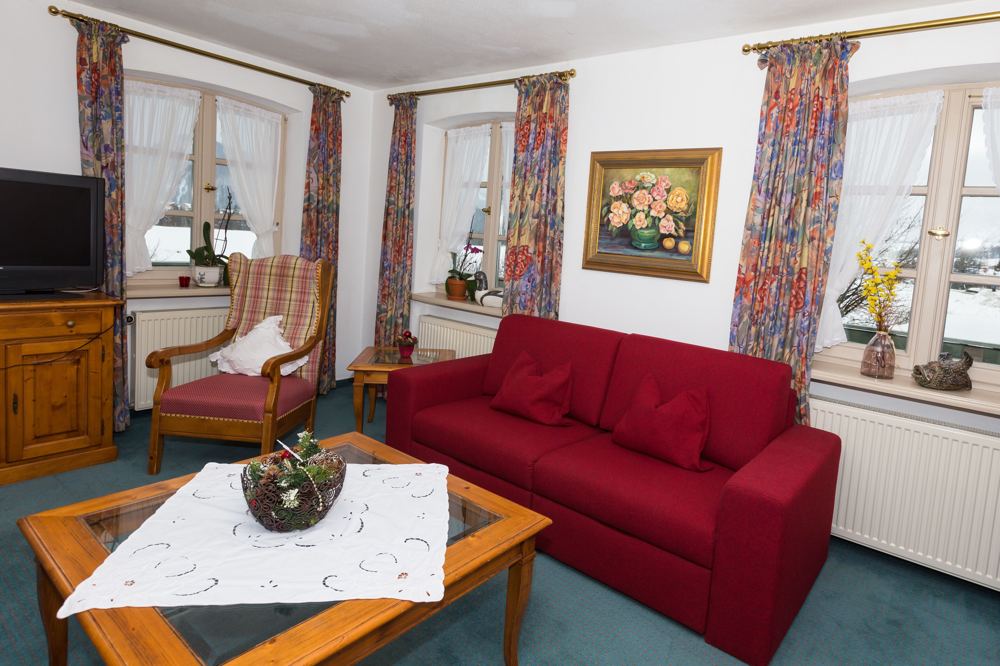 Un salon avec un canapé rouge, une table basse en bois, un fauteuil à motifs et un téléviseur posé sur un meuble en bois.