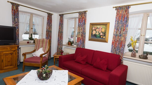 Una sala de estar con un sofá rojo, una mesa de centro de madera, un sillón escocés y un televisor sobre un mueble de madera.