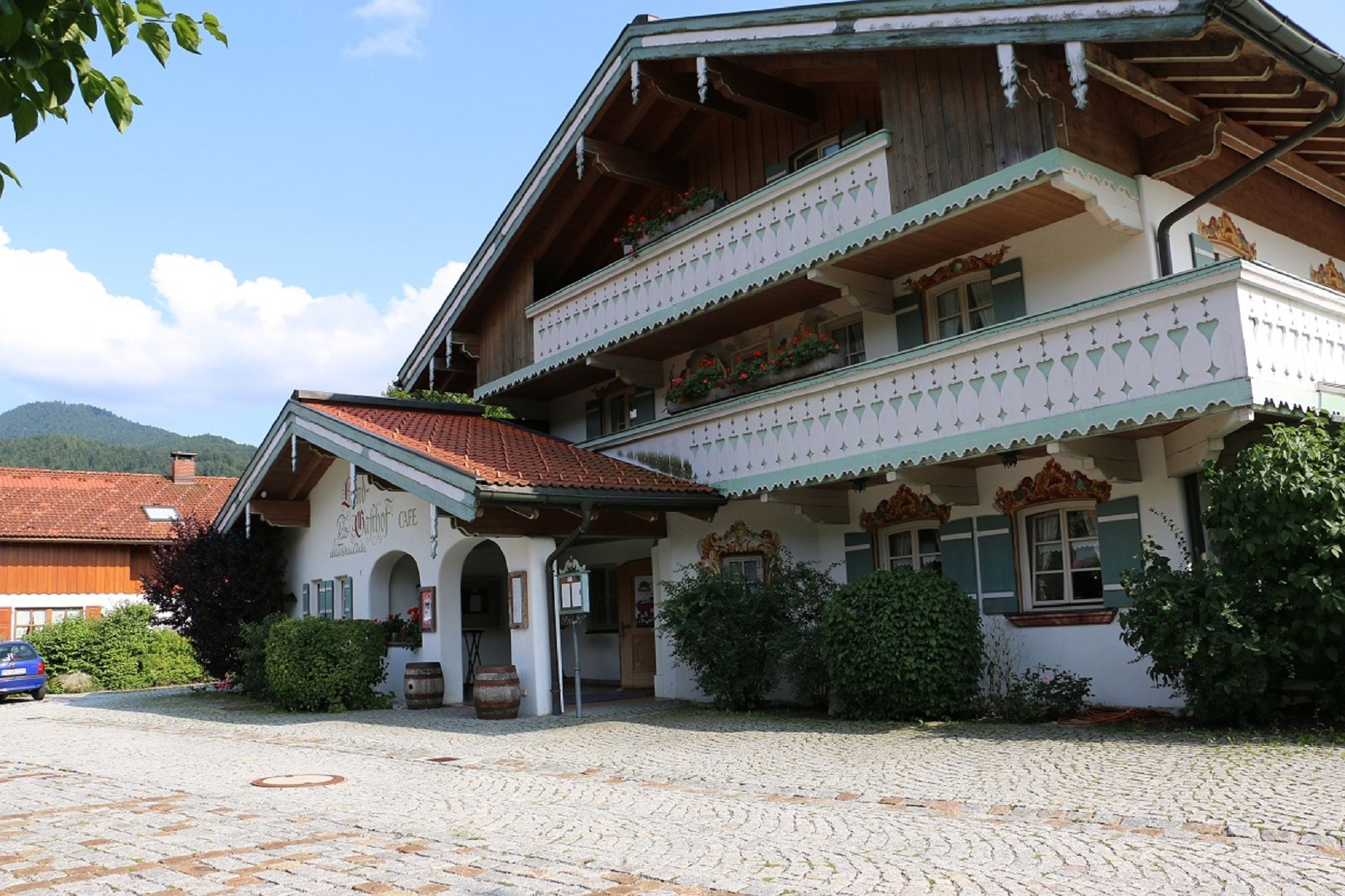 A traditional Alpine-style building with a cobblestone courtyard, wooden balconies, and a sign indicating a cafe.