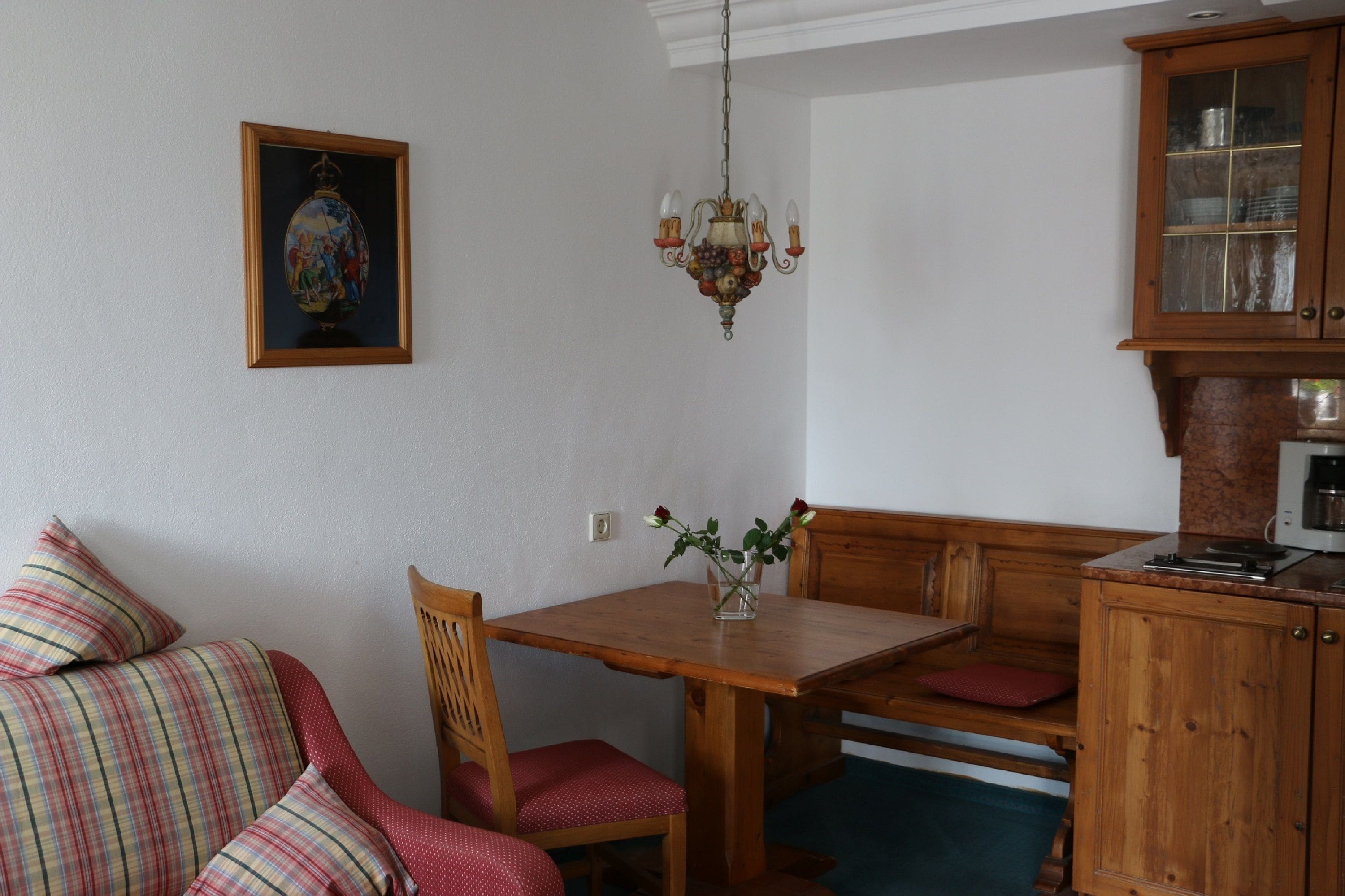 A dining area with a wooden table, chairs, and a bench. There is a chandelier hanging from the ceiling and a cabinet with glass doors.