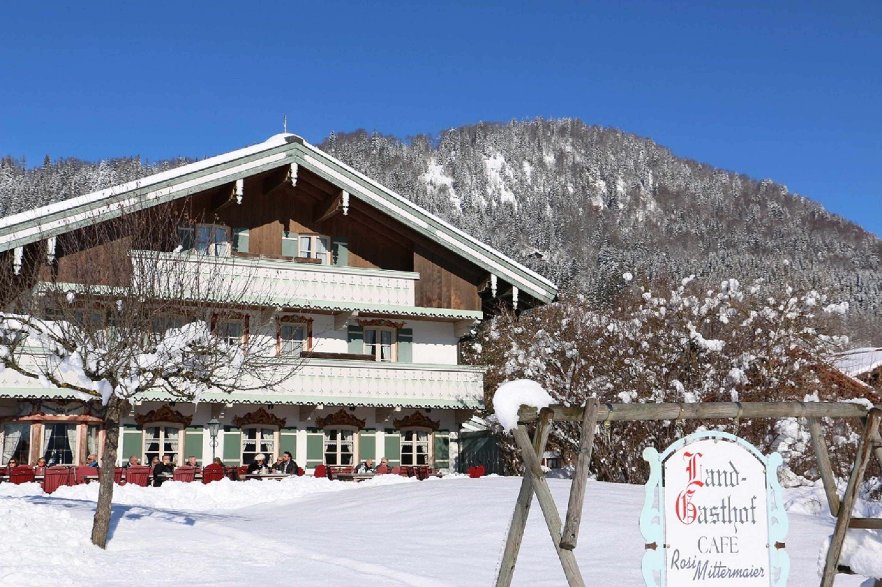 A two-story building with a sloped roof, a signboard reading "Landgasthof Cafe," and a mountainous backdrop.