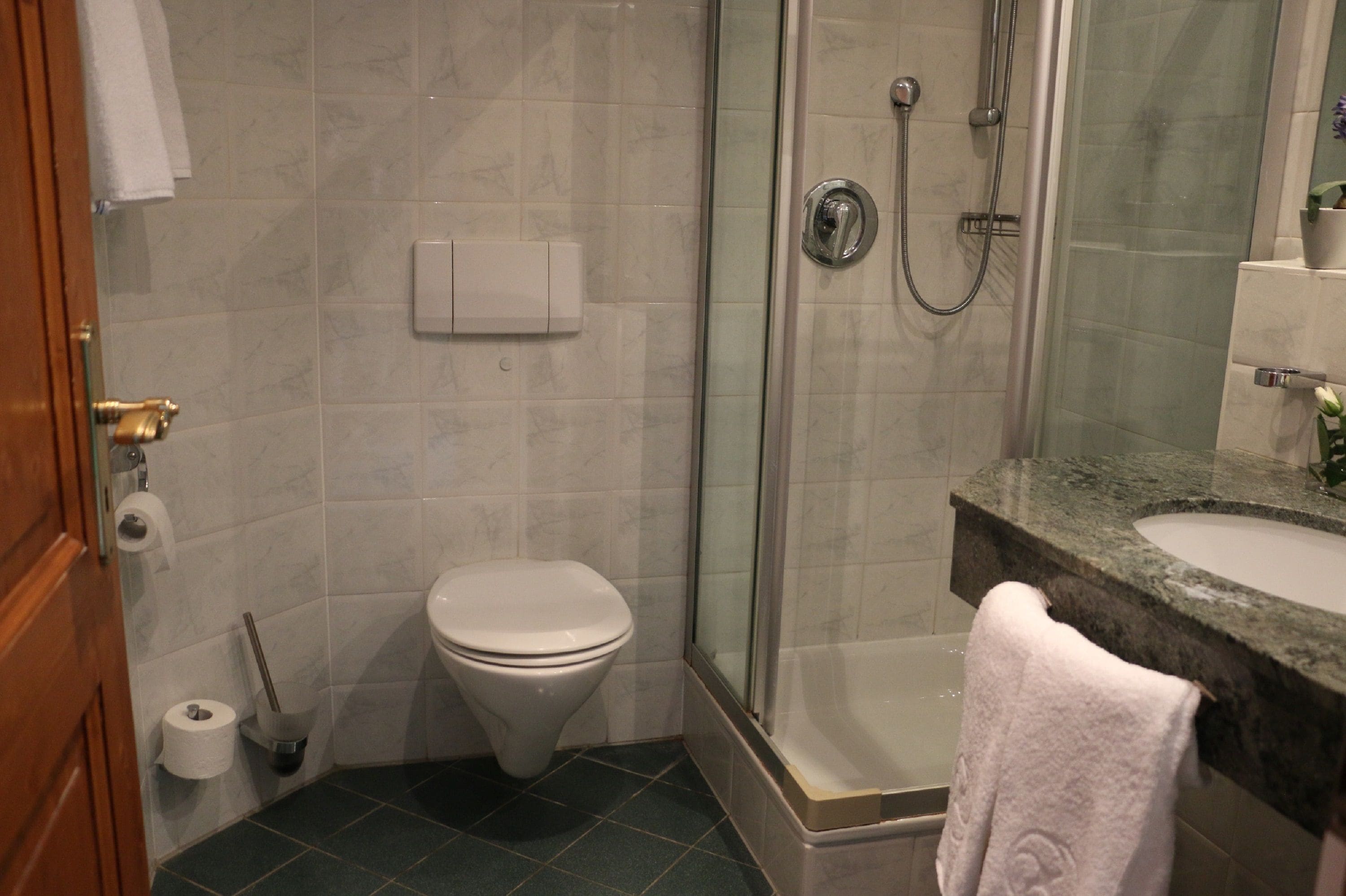 Un baño con inodoro, ducha, lavabo y una toalla colgada en la pared.