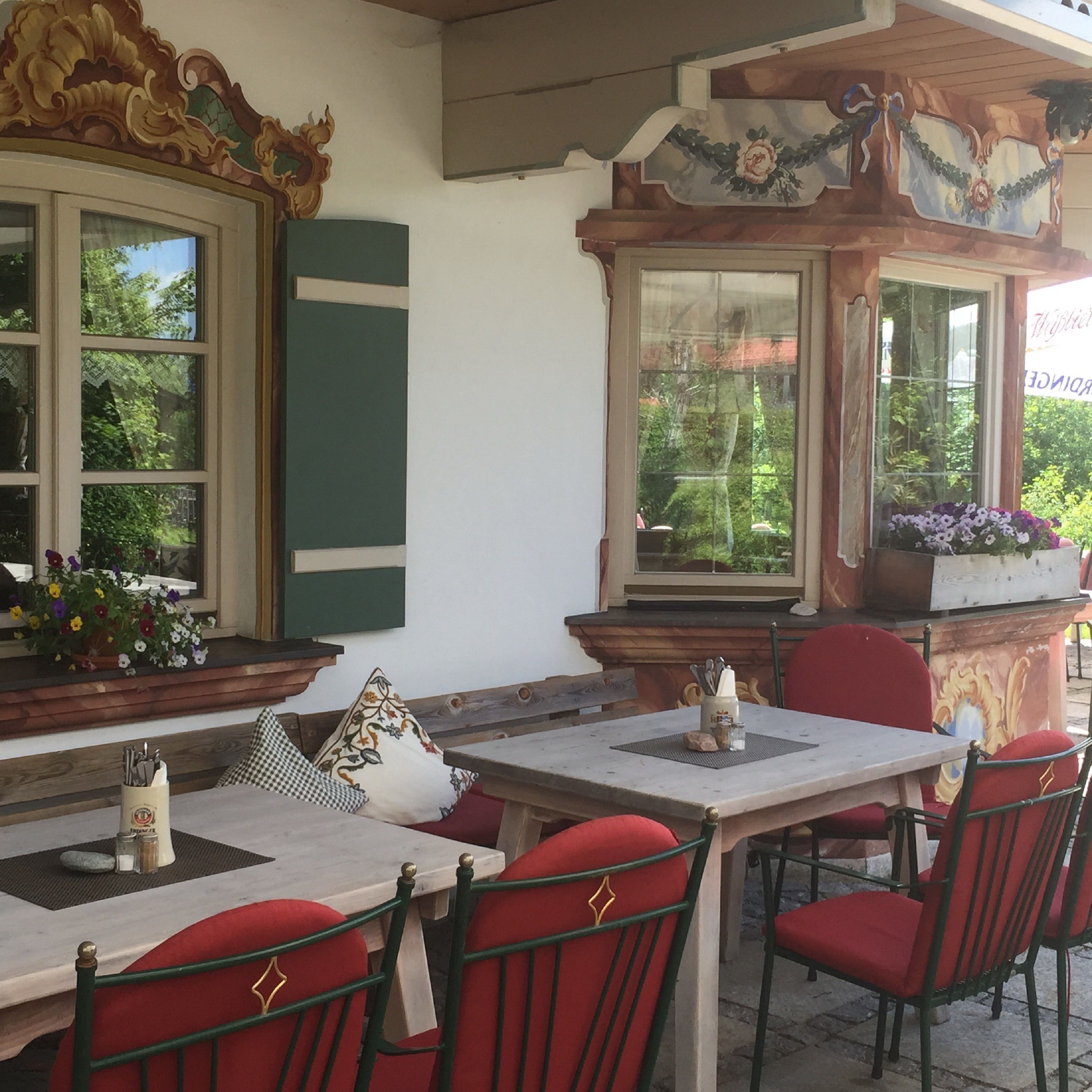 Un espacio al aire libre con mesas y sillas, ventanas amplias con marcos decorativos y vistas a zonas verdes.