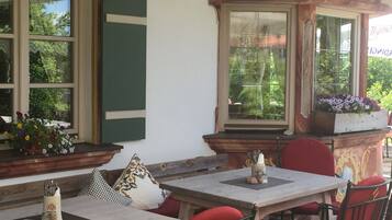 Un espacio al aire libre con mesas y sillas, ventanas amplias con marcos decorativos y vistas a zonas verdes.