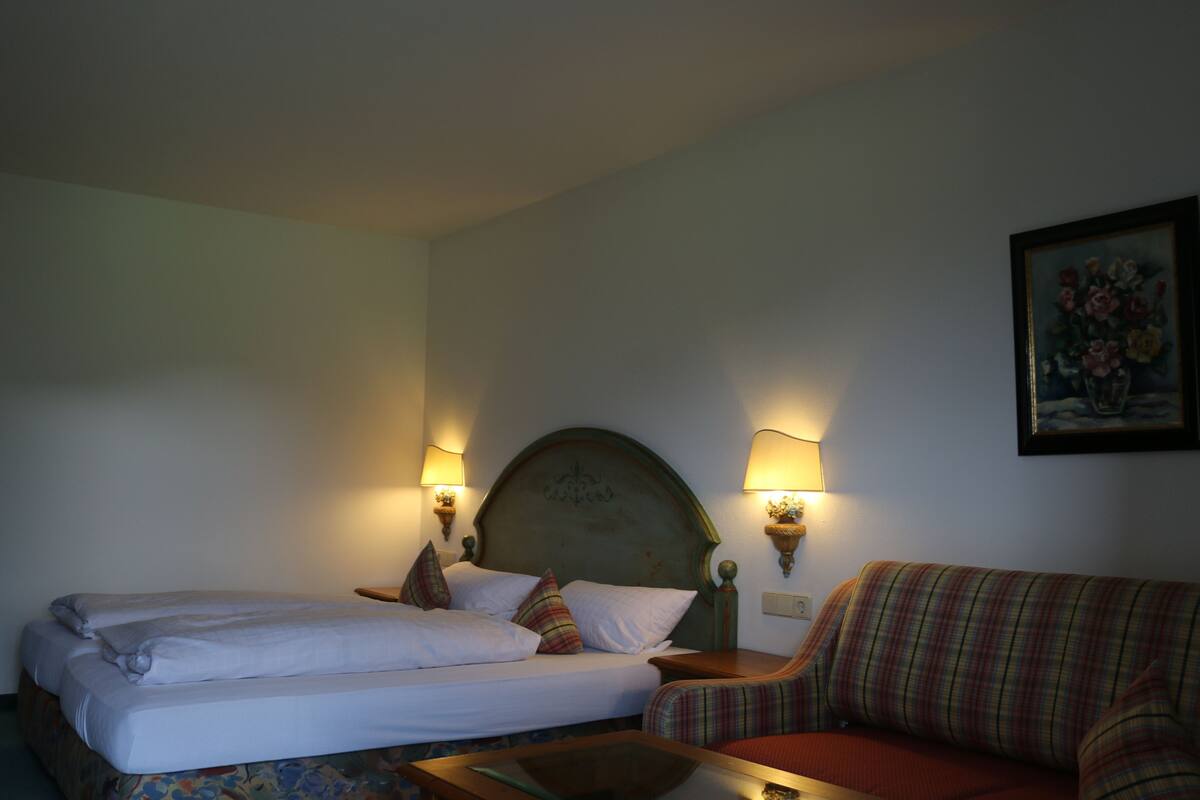 A hotel room with a bed, a sofa, and two wall-mounted lamps.