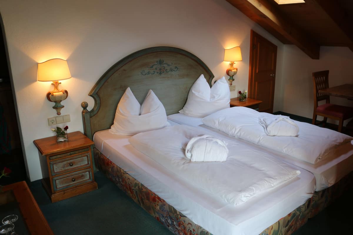 A double bed with white linens and pillows, two bedside tables with lamps, and a floral-patterned bedspread.