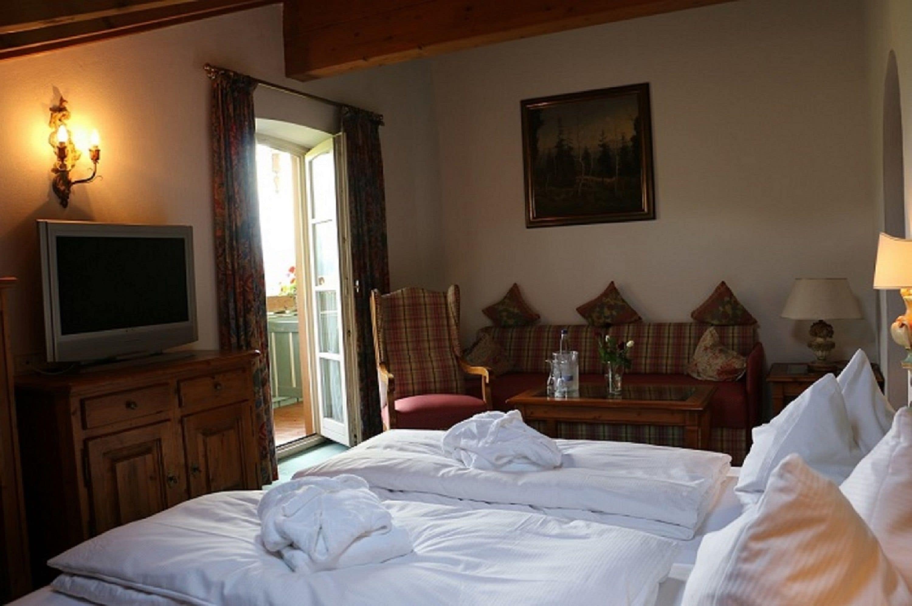 Una habitación de hotel con cama, televisión, una mesa con lámpara, una silla y un cuadro en la pared.