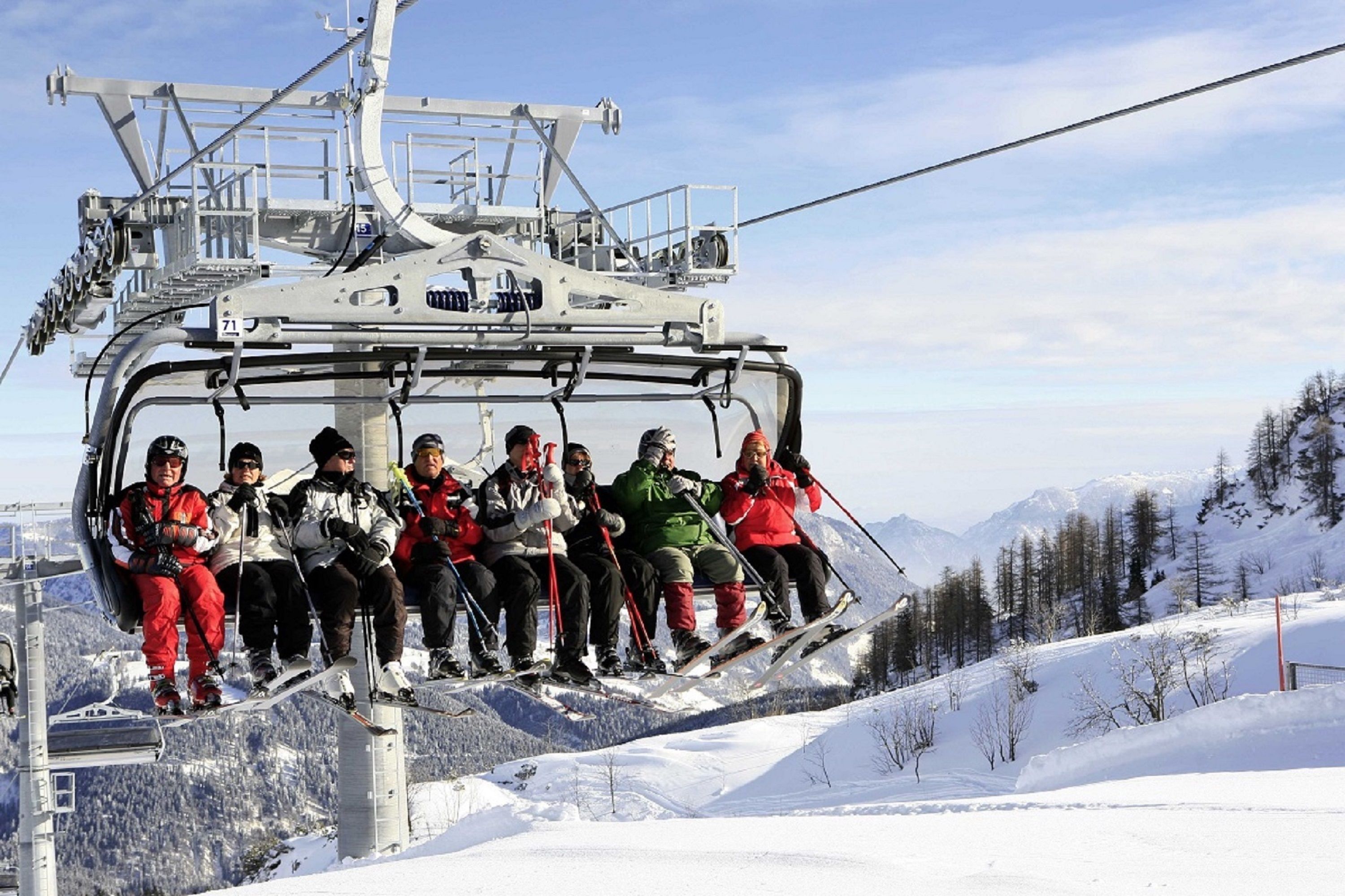 Eine Gruppe von Personen auf einer Seilbahn vor einer gebirgigen Landschaft.