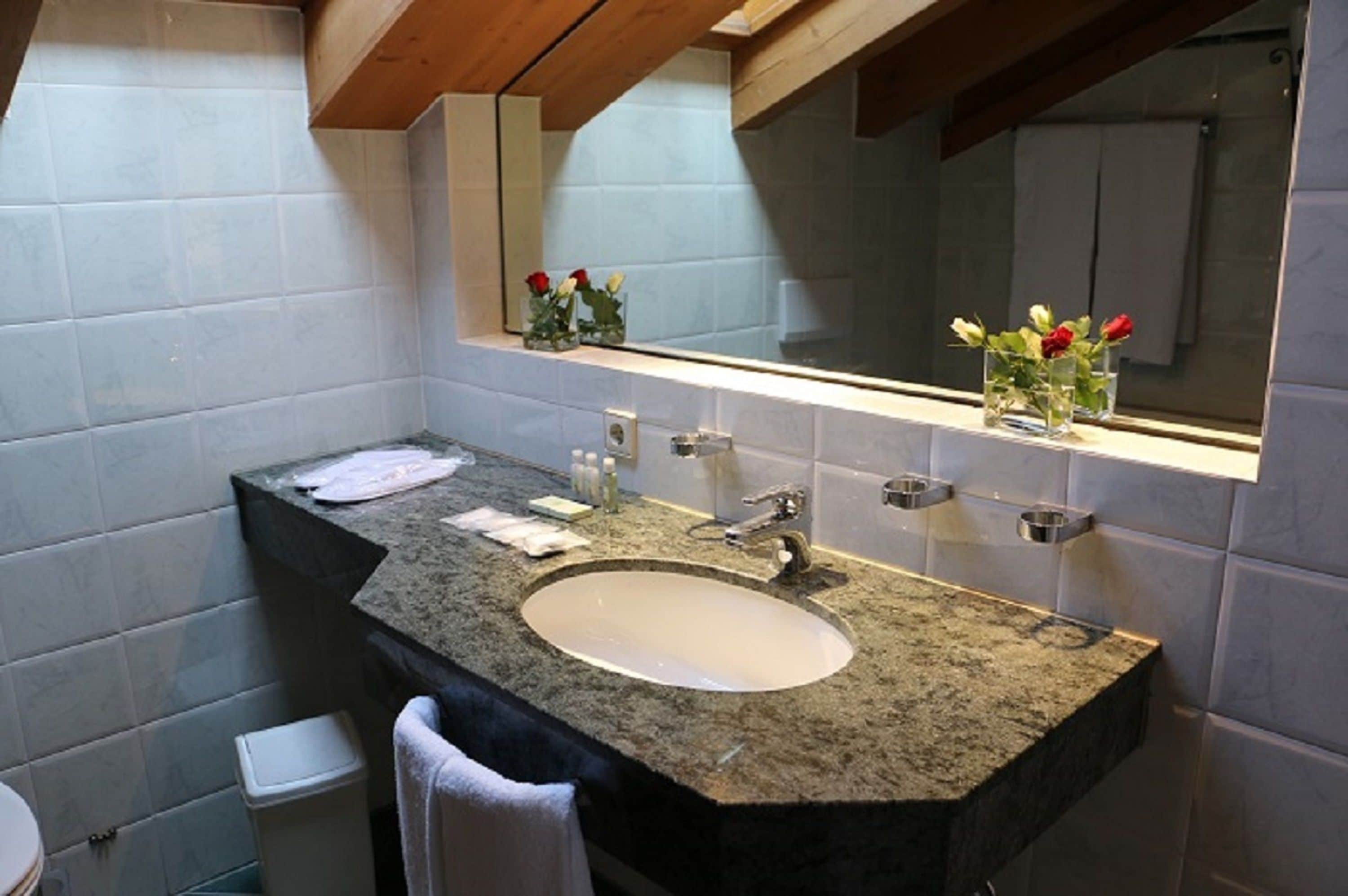 A bathroom with a granite countertop sink, a mirror, and a shelf with vases of flowers.
