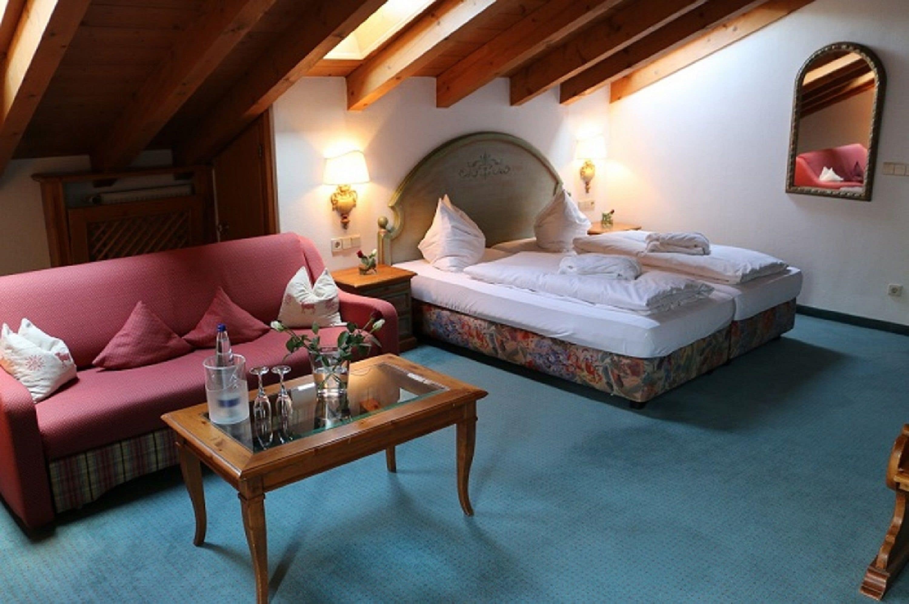 Una stanza accogliente con soffitto in legno, un letto con lenzuola bianche, un divano rosa e un tavolino da caffè in vetro.