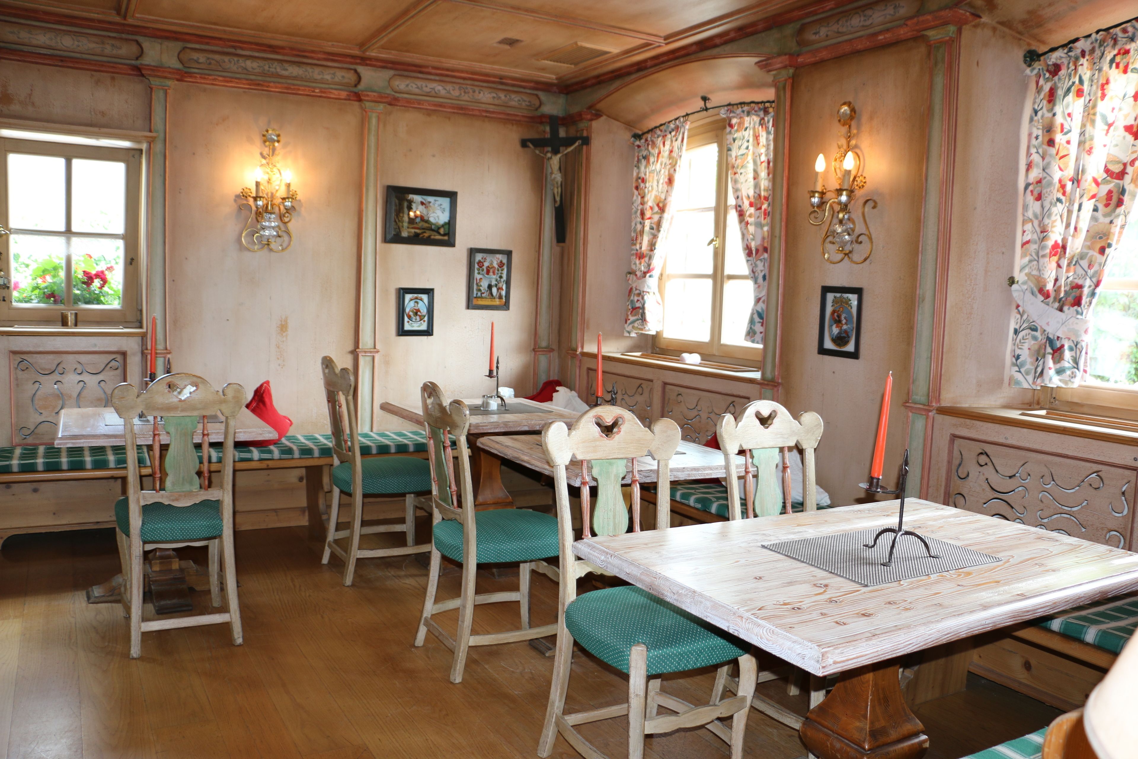 A dining area with wooden tables and chairs, a chandelier, and floral curtains.
