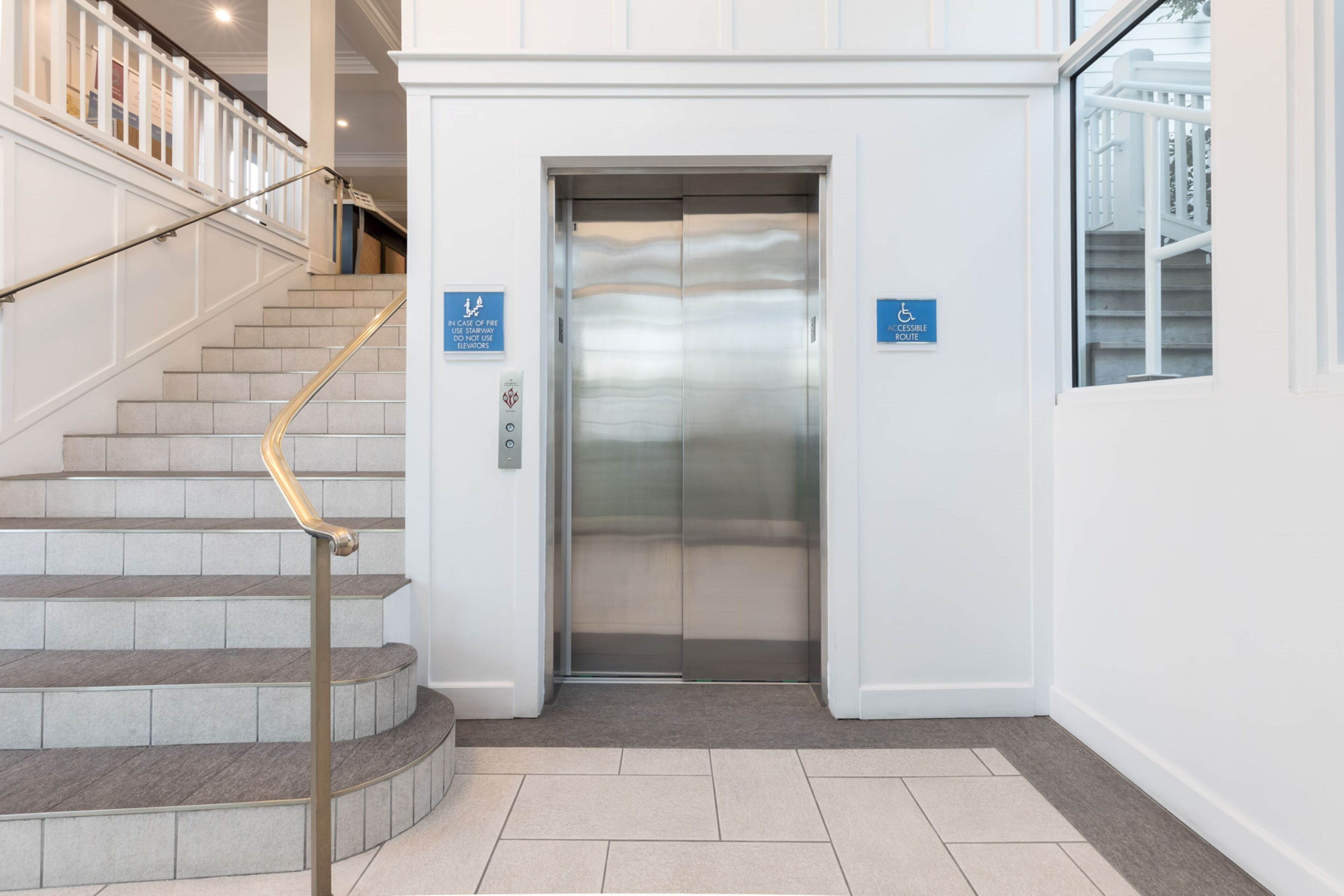 A modern elevator with a stainless steel finish, a handrail, and two blue accessibility signs.