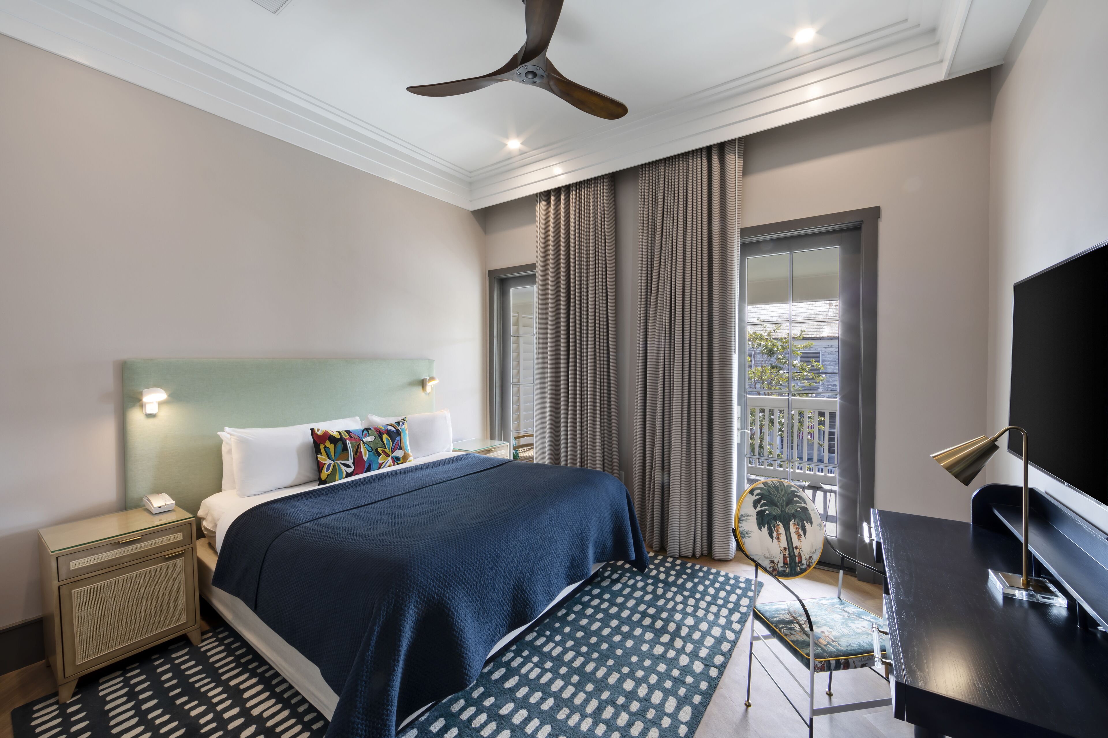 A modern hotel room with a large bed, a desk, a television, and a view of the outdoors.