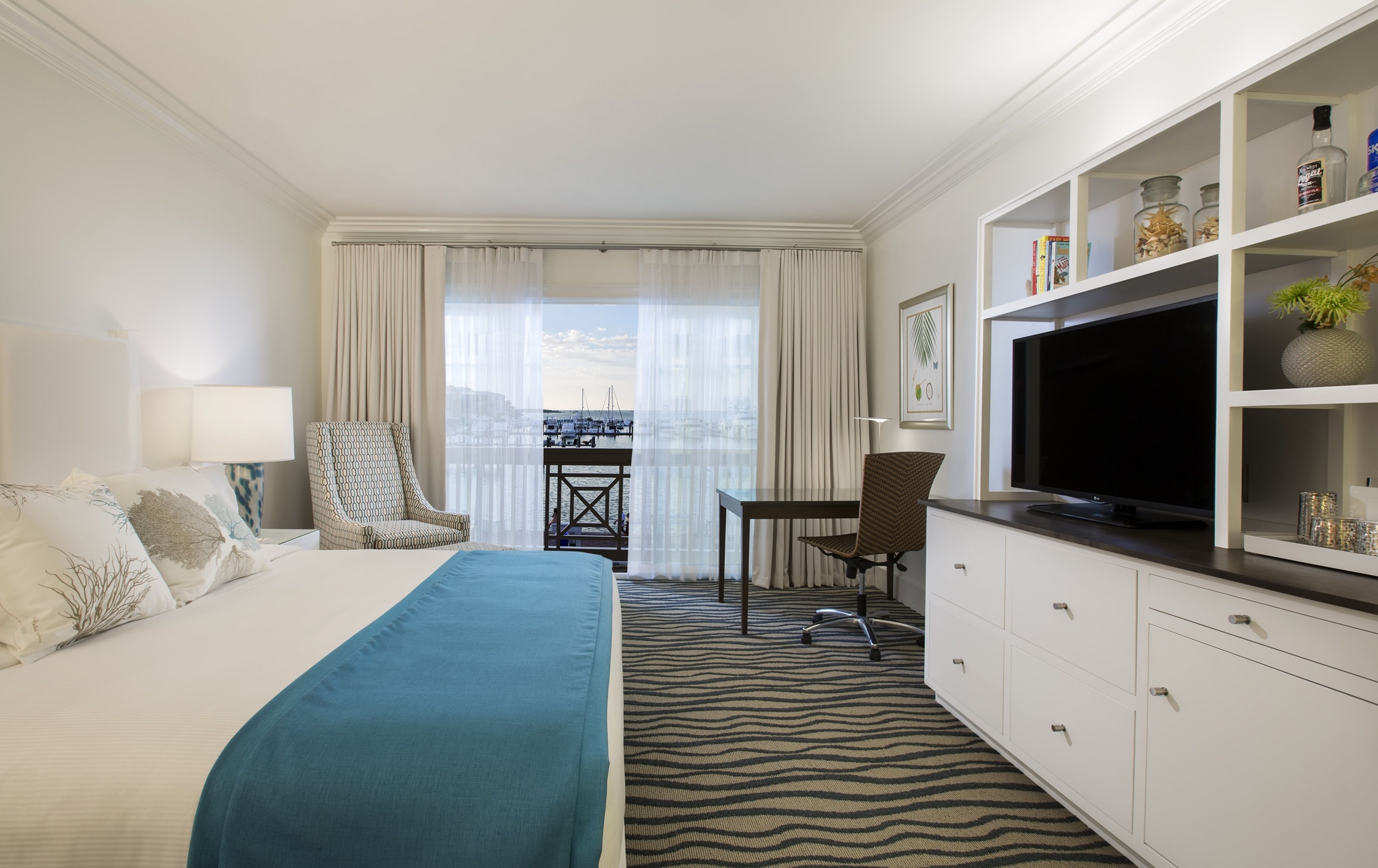 A hotel room with a bed, a TV, a desk, and a view of the city.