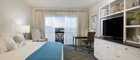 A hotel room with a bed, a TV, a desk, and a view of the city.
