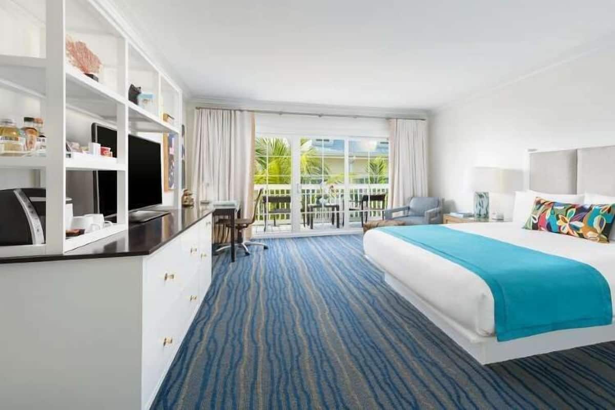 A hotel room with a bed, a desk with a computer, a chair, and a view of the outdoors.