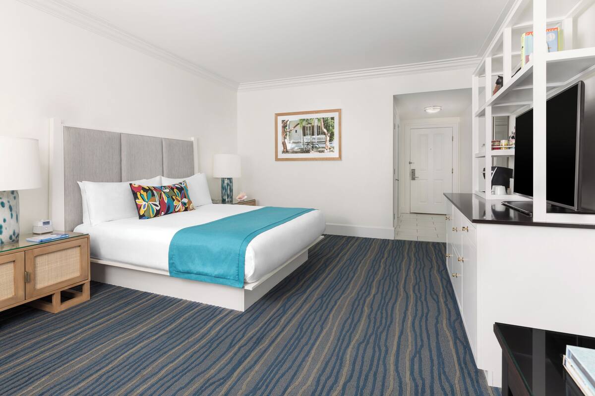A hotel room with a bed, bedside table, lamp, and a television.