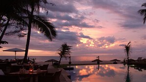 A sunset view over a calm pool with lounge chairs and umbrellas. - Amata Resort & Spa (Ngapali)