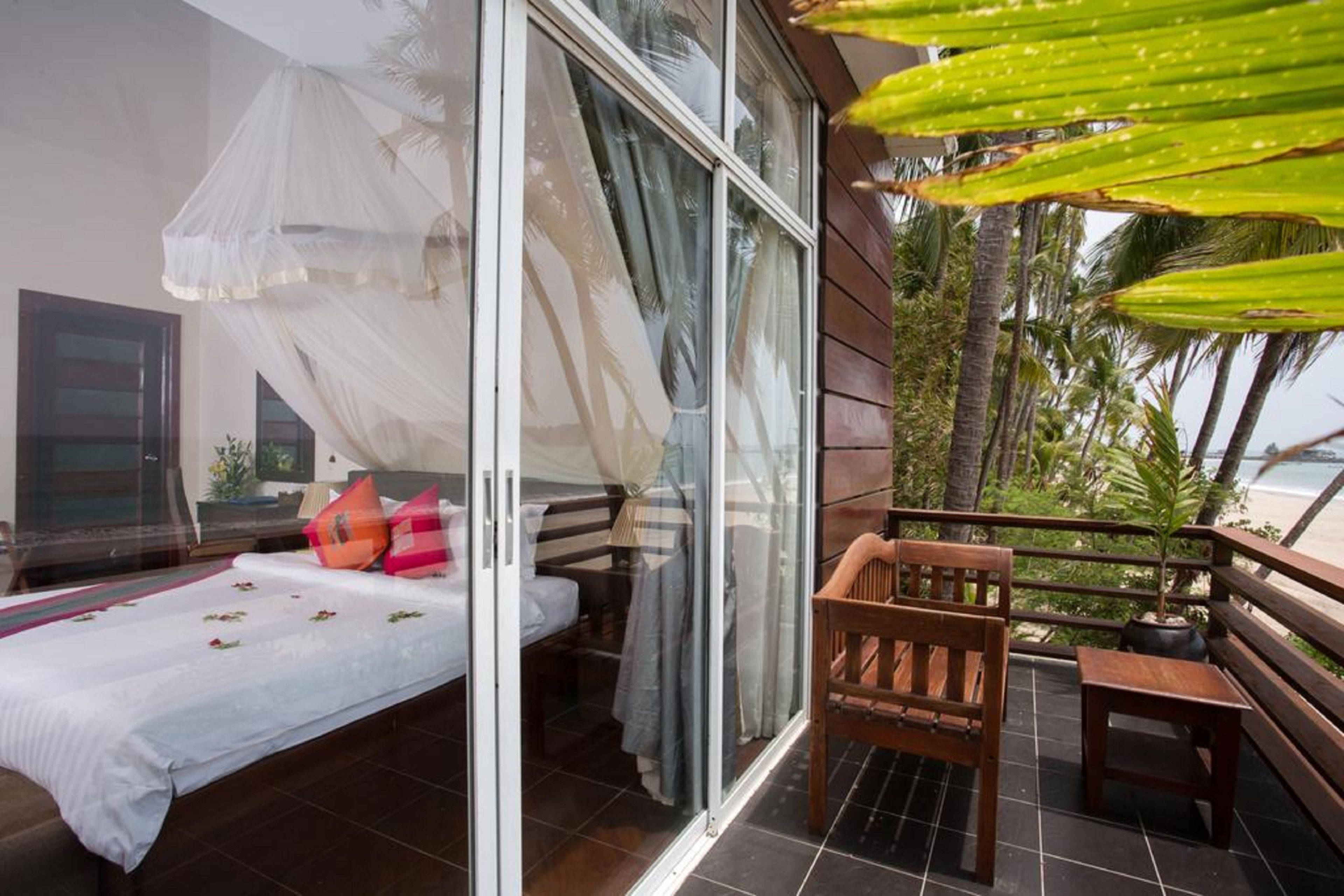 Un dormitorio con cama, mesita de noche y ventana con vistas a palmeras y al océano.